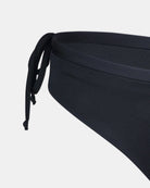 Nahaufnahme der Seite der Tide Surf Bikini Hose von Main Design in Schwarz, mit verstellbarem Kordelzug-Bund und frecher Bedeckung, gezeigt vor einem einfarbig weißen Hintergrund.