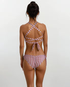 Eine Frau mit hochgestecktem Haar steht mit dem Rücken zur Kamera. Sie trägt die Main Design Blush Surf Bikinihose aus chlorresistentem Stoff mit überkreuzten Trägern und einer Schleife am Rücken. Der Hintergrund ist hell und schlicht.