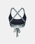 Rückenansicht des Charm Surf Bikini-Oberteils von Main Design, mit gekreuzten Trägern und einem Bindeband im unteren Rückenbereich. Hergestellt aus chlorresistentem Stoff in Marineblau mit hellblau und schwarz gepunkteten Trägern und Besätzen.