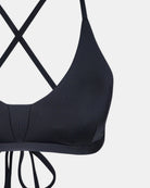 Eine Nahaufnahme des Drift Surf Bikini Oberteils von Main Design in schwarz, mit dünnen, gekreuzten Rückenträgern, die unten gebunden werden, aus nachhaltigen Materialien und auf weißem Hintergrund.