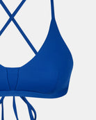 Nahaufnahme des Main Design Drift Surf Bikini Oberteils in Blau, mit überkreuzten Rückenträgern und einem Bindeverschluss, hergestellt aus nachhaltigen Materialien. Ein Teil dieses surftauglichen Oberteils ist vor einem weißen Hintergrund abgebildet.