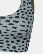 Nahaufnahme des Hale Bikini-Oberteils von Main Design mit blau-grauem Hintergrund, unregelmäßigen schwarzen Tiermotiven und einem olivgrünen linken Träger.