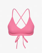 Das rosa Pasta-Bikini-Oberteil von Main Design hat dünne, überkreuzte Träger auf der Rückseite und eine Schleife vorne. Es besteht aus glattem, dehnbarem, chlorbeständigem Stoff und recycelten Materialien für eine bequeme Passform vor dem schlichten weißen Hintergrund.