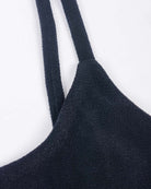 Nahaufnahme des Sassy Bikini-Tops von Main Design aus strukturiertem schwarzem Recyclingstoff mit dünnen Trägern vor weißem Hintergrund. Die raue, taktile Oberfläche des Kleidungsstücks verkörpert mühelos den Stil eines Sassy Bikini-Tops.