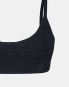 Nahaufnahme des Sassy Glitter Bikini Oberteils von Main Design in Schwarz, mit ärmellosem Rundhalsausschnitt und aus recyceltem Bikini-Stoff. Nur ein Teil des Bralettes und ein Träger sind vor dem weißen Hintergrund zu sehen.
