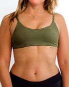 Eine Frau trägt das Main Design Sassy Bikini-Top in Olivgrün mit schwarzer Unterhose vor einem schlichten weißen Hintergrund. Ihr Gesicht ist teilweise außerhalb des Rahmens und ihr Haar ist offen, was einen nachhaltigen Look zeigt.