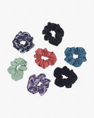 Eine Kollektion aus sieben Haargummis aus Stoffresten, die verstreut auf weißem Hintergrund angeordnet sind. Die nachhaltigen Haargummis einfarbig von Main Design sind in verschiedenen Farben erhältlich, darunter Hellgrün, Lila mit Batikmuster, Rot, Schwarz, Blaugrün und Dunkelblau.