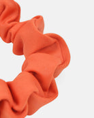 Nahaufnahme eines leuchtend orangefarbenen Haargummi einfarbig von Main Design mit geraffter, gekräuselter Lycrastoff-Textur vor einem schlichten weißen Hintergrund.