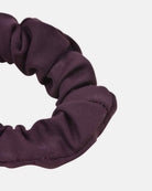 Eine Nahaufnahme eines dunkelvioletten Haargummi einfarbig von Main Design, gefertigt aus gerafftem Stoff, vor einem schlichten weißen Hintergrund.