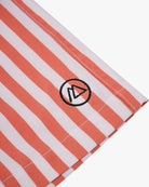 Nahaufnahme eines Stoffes mit weißen und orangefarbenen Längsstreifen aus 4-Wege-Stretch für mehr Flexibilität. Ein kleines, kreisförmiges Logo mit einem stilisierten „A“ ist aufgestickt. Perfekt geeignet für die Lean Boardshorts für Jungen von Main Design, ist der Saum an der Unterkante sichtbar.