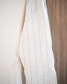 Der Kimono Soleil von Main Design aus 100% Baumwolle mit cremefarbenem Streifenmuster hängt auf einer Holzfläche mit sanftem natürlichem Licht.