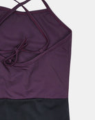 Eine Nahaufnahme des Lena Mädchen Badeanzugs von Main Design mit dünnen, überkreuzten Trägern, einem Bindeband auf dem Rücken und einem dunkelviolett-schwarzen Colorblock-Design aus recycelten Materialien, flach auf eine weiße Fläche gelegt.