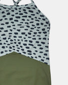 Nahaufnahme des Lena Mädchen Badeanzugs von Main Design, hergestellt aus recycelten Materialien. Er hat überkreuzte Träger, ein weiß-schwarzes, abstrakt gepunktetes Oberteil und ein einfarbiges, olivgrünes Unterteil.