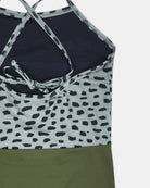 Eine Nahaufnahme des Lena Mädchen Badeanzugs von Main Design mit überkreuzten Trägern, einem schwarz-weiß gepunkteten Oberteil und einem unifarbenen, olivgrünen Unterteil. Er ist aus recycelten Materialien gefertigt.