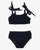 Ein schwarzer, nachhaltiger Badeanzug auf weißem Hintergrund. Der Mia Mädchen Bikini von Main Design besteht aus einem Oberteil mit zu Schleifen gebundenen Schulterträgern und einem hoch taillierten Unterteil im Standard-Bikini-Stil.