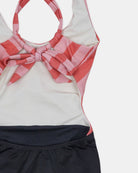 Eine Nahaufnahme des Milly Mädchen Badeanzugs von Main Design zeigt eine rosa und rot karierte Schleife am Ausschnitt, ein weißes Oberteil und ein schwarzes Unterteil. Dieser Badeanzug mit UPF50+ ist auf einem flachen weißen Hintergrund abgebildet.
