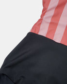 Die Nahaufnahme des Milly Mädchen Badeanzugs von Main Design zeigt korallen- und rosafarbene Längsstreifen über einem einfarbig schwarzen Teil. Die hochwertige Naht unterstreicht diesen UPF50-Badeanzug, ideal für Kinderbademode Schweiz.