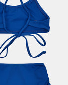 Nahaufnahme des Nalu Mädchen Bikini von Main Design in leuchtendem Blau mit Trägern zum Binden im Rücken und passendem Höschen auf weißem Hintergrund. Hergestellt aus recycelten Materialien mit UPF 50+ Sonnenschutz für ganztägigen Schutz.