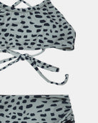 Nahaufnahme des Nalu Mädchen Bikini von Main Design, hergestellt aus recycelten Materialien mit blaugrauer Basis und schwarzen Punkten. Das Neckholder-Oberteil wird im Nacken gebunden und das Set bietet einen Sonnenschutz von UPF 50+.
