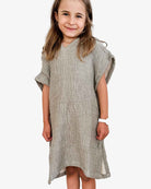 Ein junges Mädchen mit langen Haaren lächelt in die Kamera. Es trägt einen locker sitzenden, strukturierten olive grünen Kinder Badeponcho Flow von Main Design aus OEKO-TEX zertifizierter Baumwolle. Sie trägt ein weißes Armband auf einem schlichten weißen Hintergrund, der ihren fröhlichen Ausdruck unterstreicht.