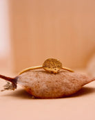 Der 24K vergoldete Ring von Adorabili und Atelier Mouti mit Igel-Design liegt auf einem braunen Blatt vor beigem Hintergrund - handgefertigt in Frankreich.