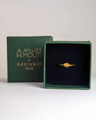 Der Ring von Adorabili und Atelier Mouti, ein zarter Ring aus 24 Karat vergoldetem Gold mit einem kleinen runden Detail, wird in einer offenen grünen Schmuckschatulle mit der Aufschrift "Atelier Mouti x Adorabili Paris" in Gold auf dem Deckel vor einem schlichten, hellen Hintergrund präsentiert.
