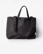 Die Stofftasche klein von OMOM by Main Design ist eine schwarze Tragetasche aus Bio-Baumwolle mit zwei kurzen Henkeln und einem langen Schulterriemen, abgebildet auf einem schlichten weißen Hintergrund.