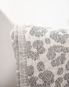 Eine Nahaufnahme des hellen Stoffes mit grauem Leopardenmuster, drapiert über Weiß - perfekt, um Ihrem Raum mit der gemütlichen Main Design Decke Savanna ein subtiles Flair zu verleihen.