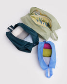 Das BAGGU 3D Zip Set von BAGGU besteht aus grünen, dunkelblauen und hellblauen Reißverschlusswürfeln auf einer weißen Oberfläche. Der grüne Würfel fasst Schuhe, die anderen haben gerollte Hemden - stilvolle Reiseutensilien für jede Reise.