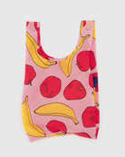 Die BAGGU Baby Tragetasche von BAGGU ist eine wiederverwendbare Tasche aus recyceltem Nylon mit einem rosa Hintergrund, der mit roten Äpfeln und gelben Bananen verziert ist. Sie hat breite Griffe, ein blaues Seitenetikett und ist perfekt für umweltfreundliches Einkaufen.