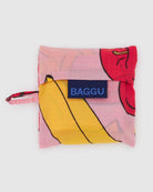 Die BAGGU Baby Tragetasche ist eine kompakte, faltbare Tasche in leuchtendem Rot und Gelb, hergestellt aus recyceltem Nylon mit einem blauen "BAGGU"-Anhänger und einer passenden Stoffschlaufe - ideal für umweltbewusste Käuferinnen und Käufer.