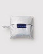 Eine silbern glänzende, quadratische BAGGU Baby Tragetasche aus recyceltem Nylon, mit einem kleinen linken Griff und einem navyfarbenen "BAGGU"-Etikett auf der Vorderseite, dargestellt auf einem schlichten weißen Hintergrund.
