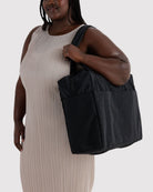 BAGGU Cloud Carry-On Tasche in Black: Schwarze Reisetasche über der Schulter getragen.
