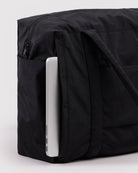 BAGGU Cloud Carry-On Tasche in Black: Seitliches Reissverschlussfach der schwarzen Reisetasche mit Laptop.