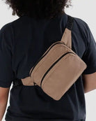 Eine Person mit schwarzem Hemd ist von hinten zu sehen, die eine braune BAGGU-Gürteltasche aus recyceltem Nylon mit einem verstellbaren schwarzen Riemen über Schulter und Rücken trägt.