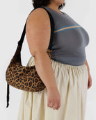 Eine Person in einem grauen ärmellosen Oberteil und einem cremefarbenen Rock trägt die BAGGU Medium Nylon Crescent Bag mit einem braunen Leopardenmuster. Der Hintergrund ist einfarbig weiß.