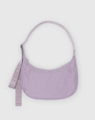 Die BAGGU Medium Nylon Crescent Bag in pastellfarbenem Lavendel hat eine geschwungene Form, einen verstellbaren Riemen und einen passenden abnehmbaren "BAGGU"-Schlüsselanhänger auf der linken Seite, der auf einem hellgrauen Hintergrund abgebildet ist.
