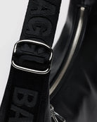 Nahaufnahme der BAGGU Medium Recycled Leather Crescent Bag in Schwarz mit einem breiten, verstellbaren Riemen mit geprägtem Text, glänzender Metallschnalle und einem teilweise sichtbaren silbernen Reißverschluss auf der glatten Oberfläche aus recyceltem Leder.