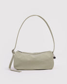 Die BAGGU Nylon Loaf Bag von BAGGU ist eine hellbeige, minimalistische Umhängetasche für Damen mit einem einzelnen Riemen, einer gewölbten Oberseite, einem silbernen Reißverschluss und einem kleinen, runden, silbernen Anhänger auf dem Griff, abgebildet auf einem schlichten weißen Hintergrund.