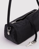 Die „BAGGU Nylon Loaf Bag“ von BAGGU ist eine schwarze, aus recyceltem Material gefertigte Umhängetasche mit rechteckiger Form, silbernem Reißverschluss, rundem Anhänger am Henkel und einem schwarzen Riemen mit zwei silbernen Schlüsseln, abgebildet vor einem hellen, neutralen Hintergrund.