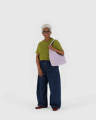 Eine ältere Frau mit kurzen weißen Haaren trägt ein grünes Hemd, weite Bluejeans, braune Schuhe und trägt eine BAGGU Nylon Shoulder Bag von BAGGU über der Schulter. Sie steht vor einem schlichten weißen Hintergrund.