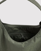 Eine Nahaufnahme einer geöffneten BAGGU-Nylon-Umhängetasche in Dunkelgrün, die den Innenraum und die innere Reißverschlusstasche zeigt, vor einem schlichten hellen Hintergrund.
