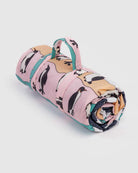 Eine aufgerollte rosa BAGGU Puffy Picknickdecke mit Griff, die ein verspieltes Pinguinmuster mit schwarzen, weißen und gelben Akzenten aufweist.