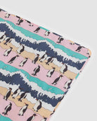 Die BAGGU Puffy Picnic Blanket zeigt einen verspielten Pinguin-Print auf pastellrosa, beigen und blauen Streifen mit blauen Wellen - perfekt als nachhaltige Picknickdecke mit Trageriemen.