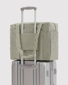Eine BAGGU Small Cloud Carry-On Tasche von BAGGU in Grün-Weiß ist am Griff eines silbernen Hartschalenkoffers befestigt - ideal als 16-Zoll-Laptoptasche oder Tasche unter dem Flugzeugsitz.