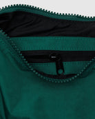 Nahaufnahme einer grünen BAGGU Small Nylon Crescent Bag, die teilweise geöffnet wurde, um eine kleinere Innentasche mit schwarzem Reißverschluss zu zeigen. Die Tasche aus recyceltem Nylon von BAGGU ist robust, wasserabweisend und perfekt für den umweltbewussten Gebrauch unterwegs.