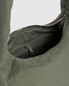 Nahaufnahme einer geöffneten BAGGU Small Nylon Meringue Bag in Olivgrün mit silbernem Reißverschluss und einer darin sichtbaren Innentasche mit Reißverschluss, abgebildet vor einem einfarbigen Hintergrund.