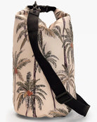 Die Dry Bag von Meraki Supply Co. by Main Design hat eine zylindrische Form und ein tropisches Design mit Palmenillustrationen auf beigem Hintergrund. Sie verfügt über einen schwarzen verstellbaren Schultergurt und einen Rollverschluss mit schwarzer Schnalle. Diese wasserdichte Tasche ist perfekt für Outdoor- und Wasseraktivitäten und hält Ihre Reiseutensilien sicher und trocken.