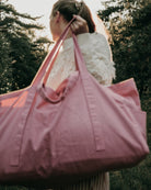 Eine Person mit langen Haaren in einem Pferdeschwanz trägt die Stofftasche gross von OMOM by Main Design über ihrer Schulter im Freien, mit Bäumen und Sonnenlicht im Hintergrund. Das Bild ist leicht unscharf.