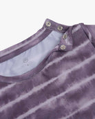 Nahaufnahme eines violetten Hemdkragens mit Batikmuster und zwei Metalldruckknöpfen, teilweise geöffnet. Das Hemd, das an ein Aina Kinder UV-Shirt von Main Design mit UPF 50+ Sonnenschutz erinnert, hat ein weißes Netz-Innenfutter aus nachhaltigem Stoff. Der Hintergrund ist weiß.